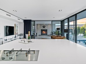 A modern living room with a fireplace, a large glass wall, and a pool view.