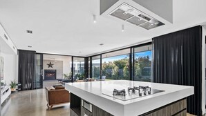 Eine moderne Küche mit einer großen Kochinsel, einem Kamin und Blick ins Freie.