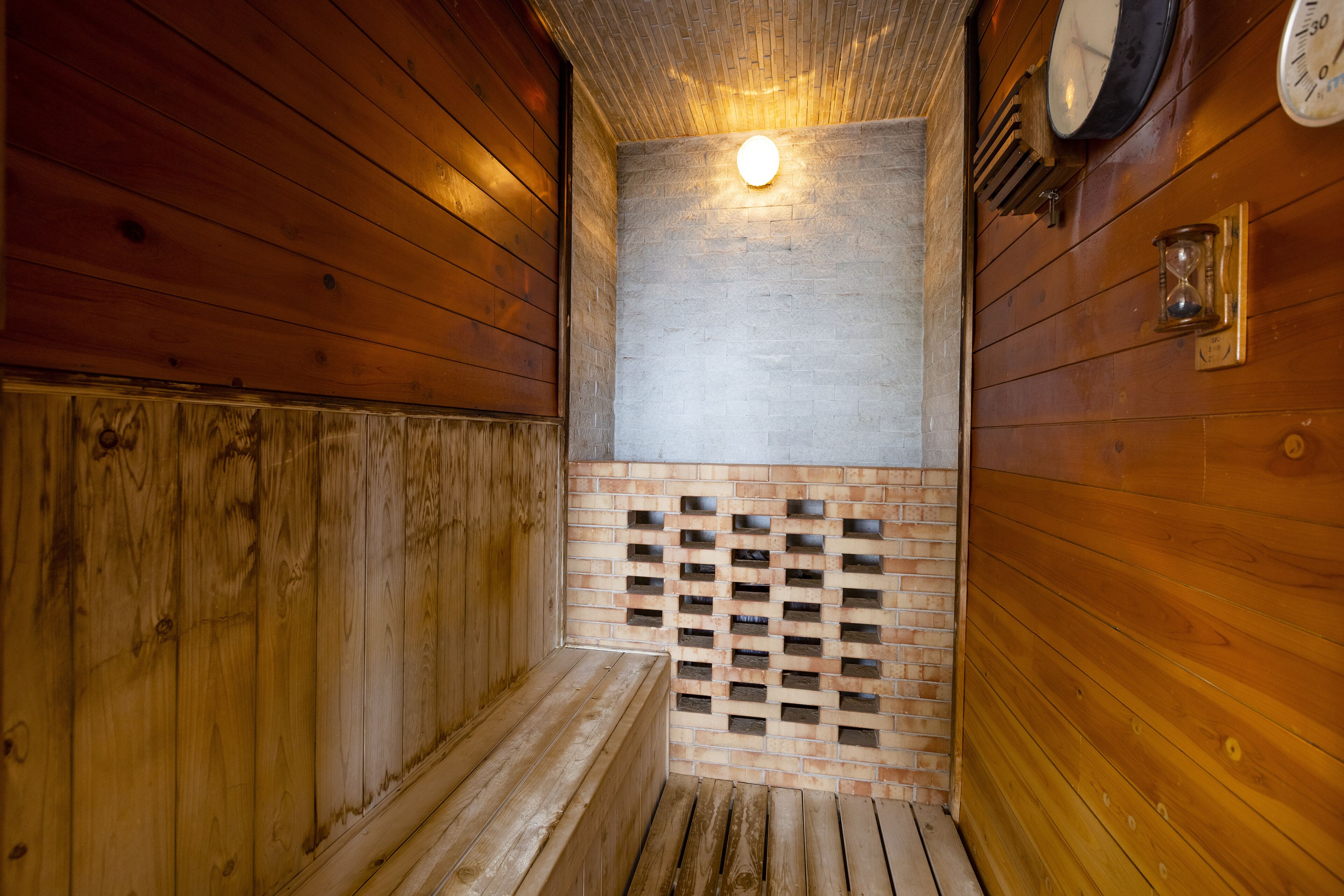 Una sauna de madera con un banco, una pared de ladrillo y una lámpara.
