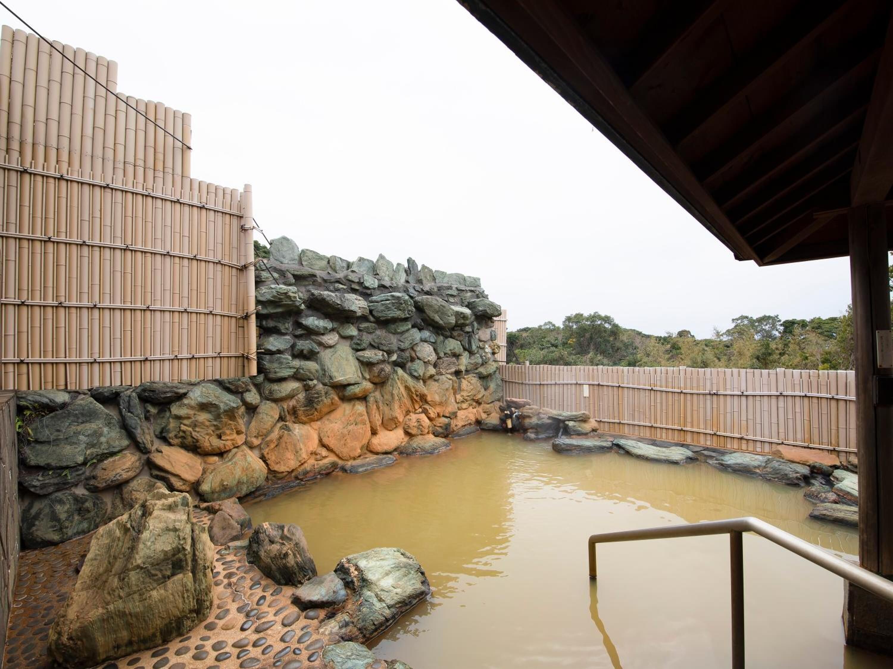 Een traditioneel Japans onsen met een stenen muur en bamboe hek, een houten terras en een klein zwembad.