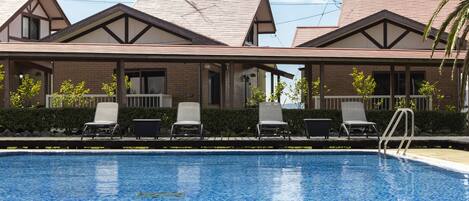 A hotel with a swimming pool, lounge chairs, and a covered patio area.