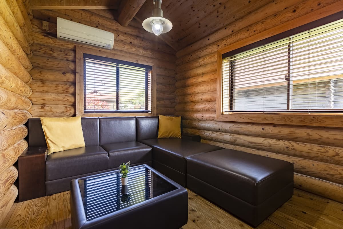 Ein Blockhauskamin mit Ecksofa, Couchtisch und großen Fenstern mit Jalousien.