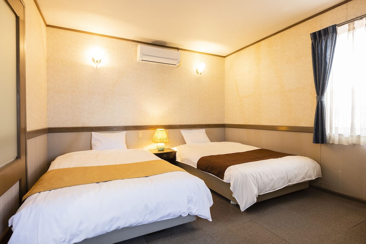Ein Hotelzimmer mit zwei Betten, einer Klimaanlage, einer Lampe und einem Fenster mit Vorhängen.