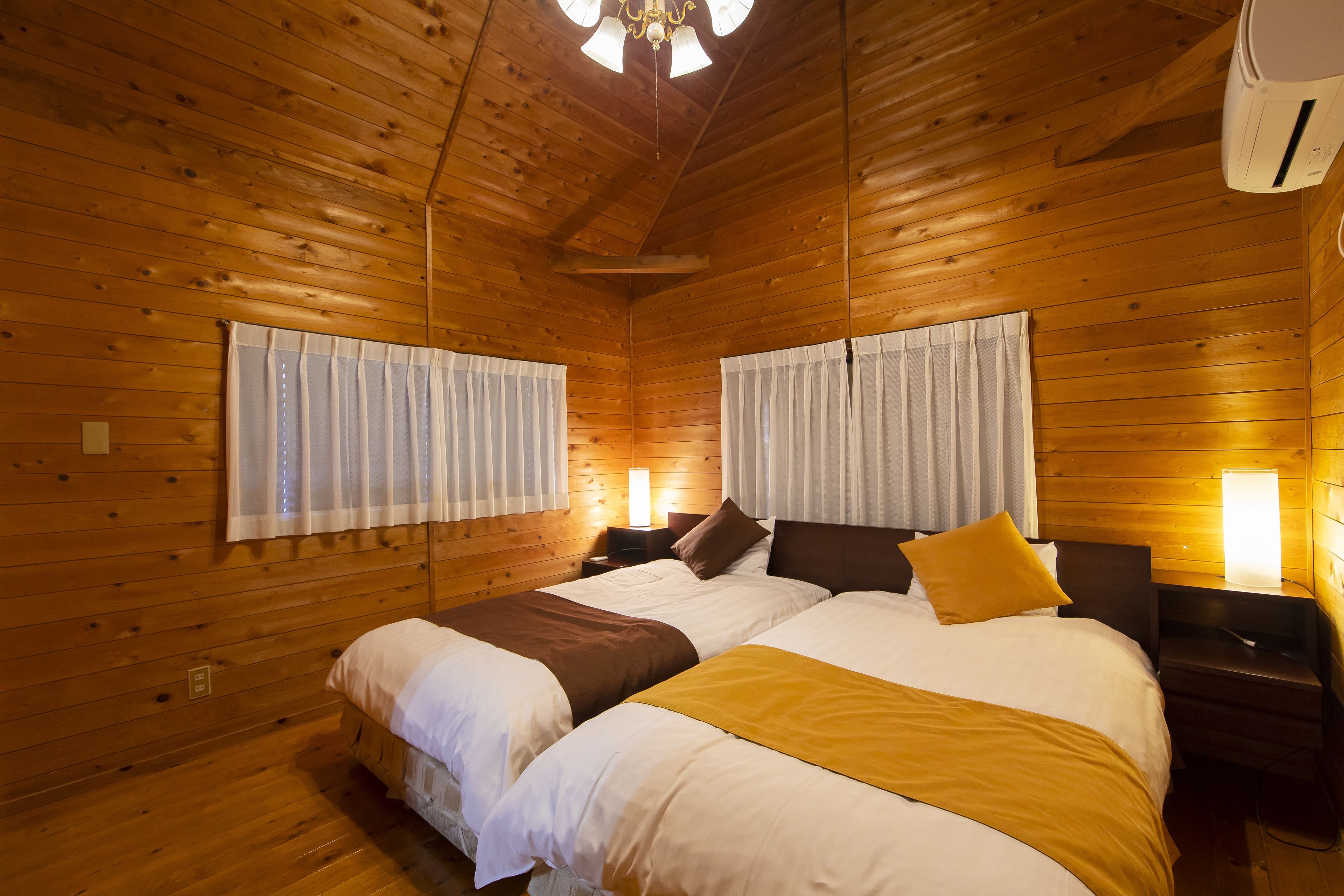 A wooden cabin bedroom with two beds, a ceiling fan, and a wall-mounted heater.