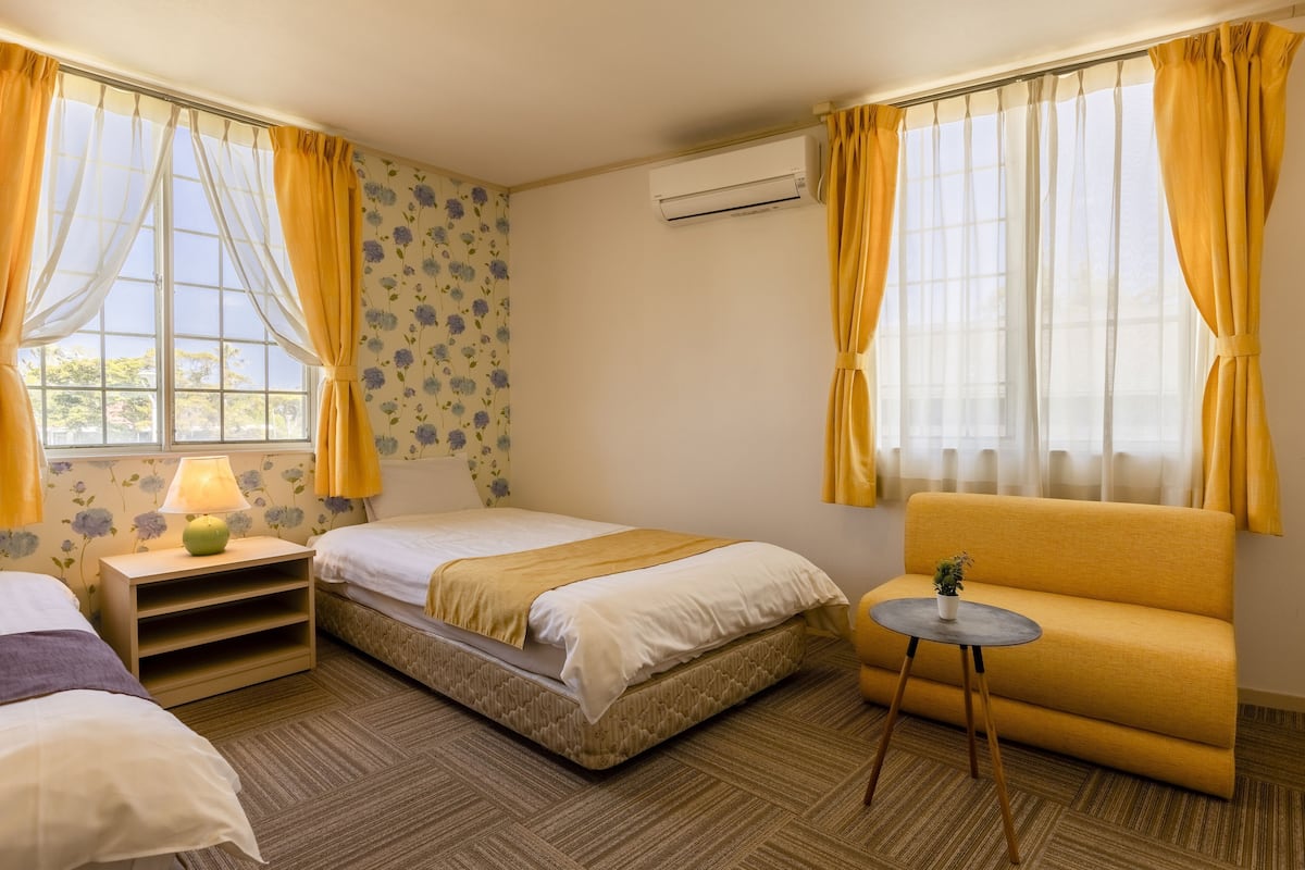 Ein Hotelzimmer mit Bett, einer Couch, einem kleinen Tisch mit Pflanze und einem fenster mit Vorhängen.