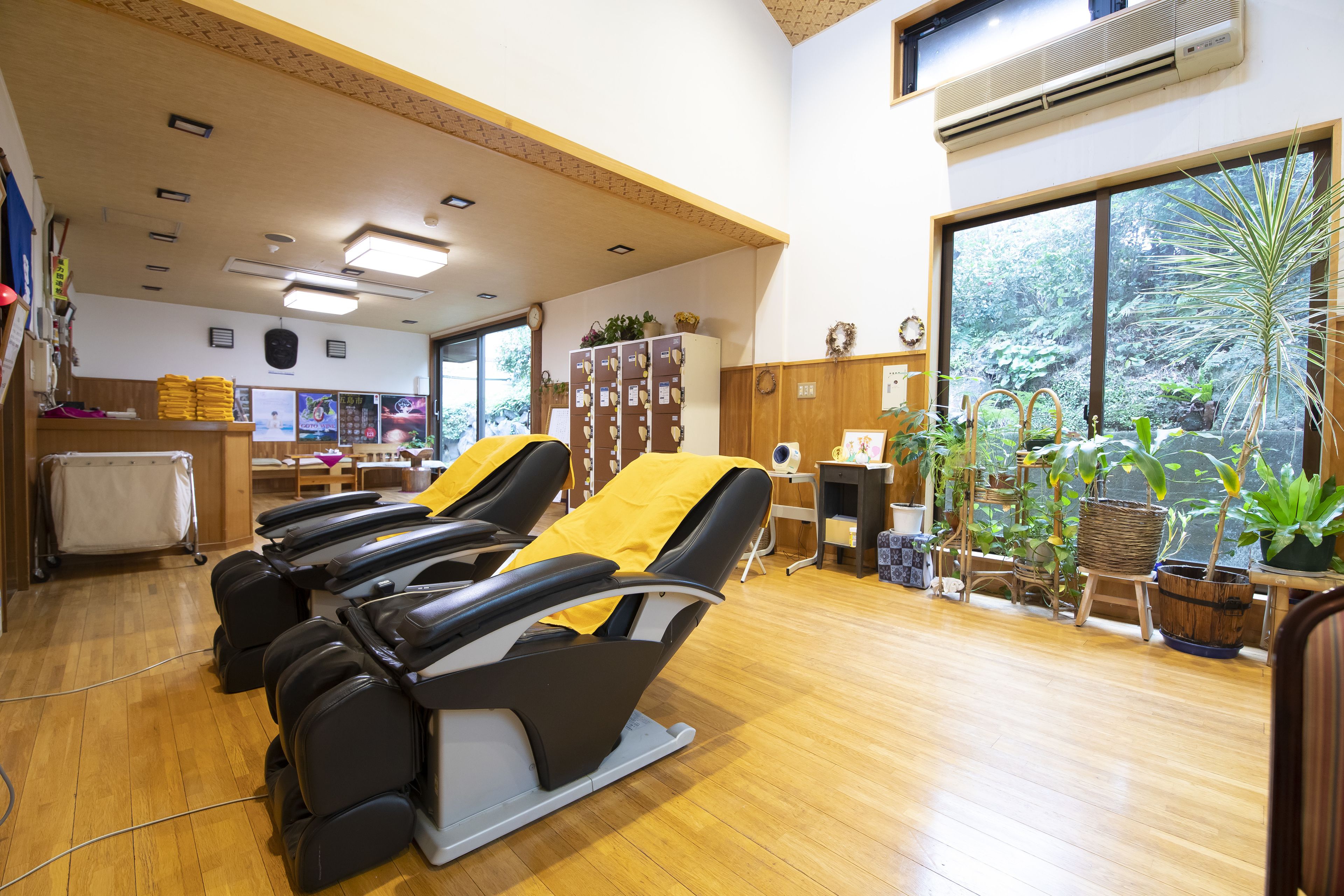 A room with massage chairs, a reception desk, and large windows with a view of greenery.