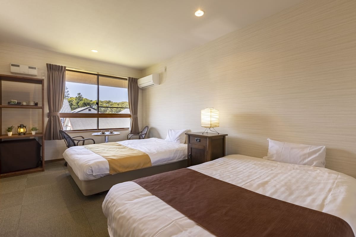 Ein Hotelzimmer mit zwei Betten, einem Schreibtisch, einem Stuhl, einer Lampe und einem Fenster mit Vorhängen.