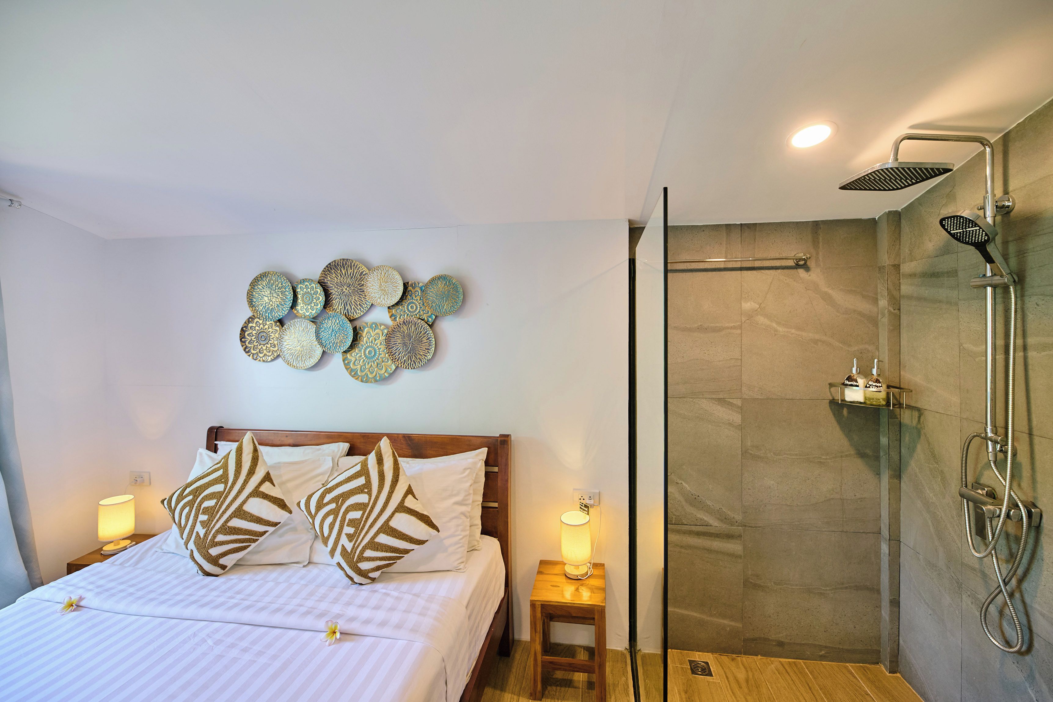 A hotel room with a bed, bedside lamps, a shower with a handheld showerhead, and decorative wall art.