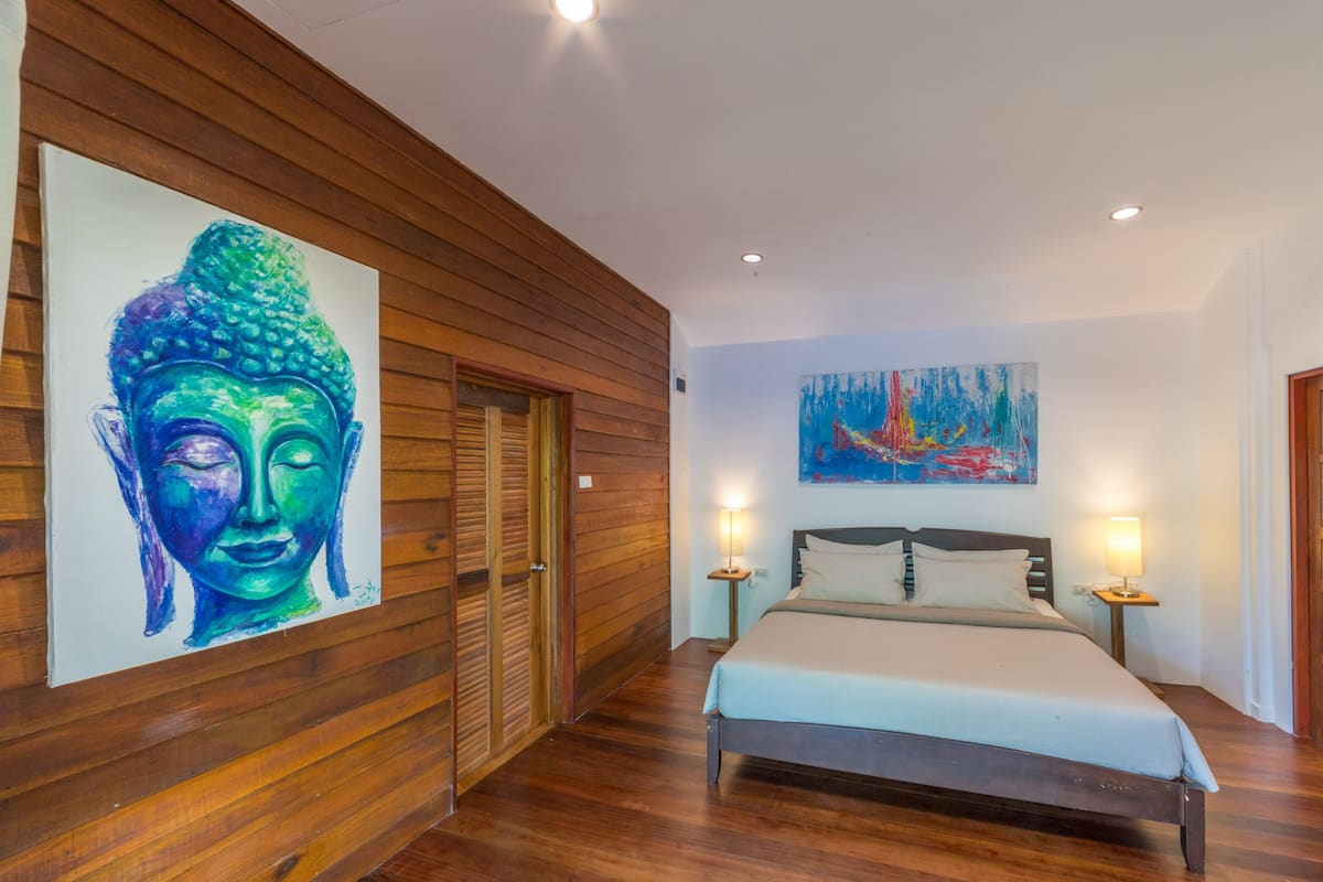 A bedroom with a wooden floor, a bed with a white bedspread, two bedside lamps, and two doors.