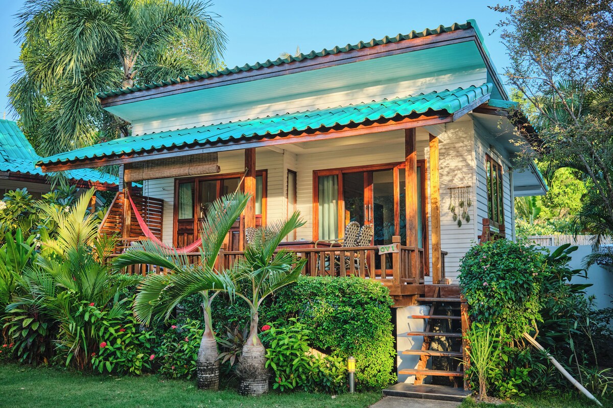 A traditional house with a porch, surrounded by lush greenery and a clear sky.