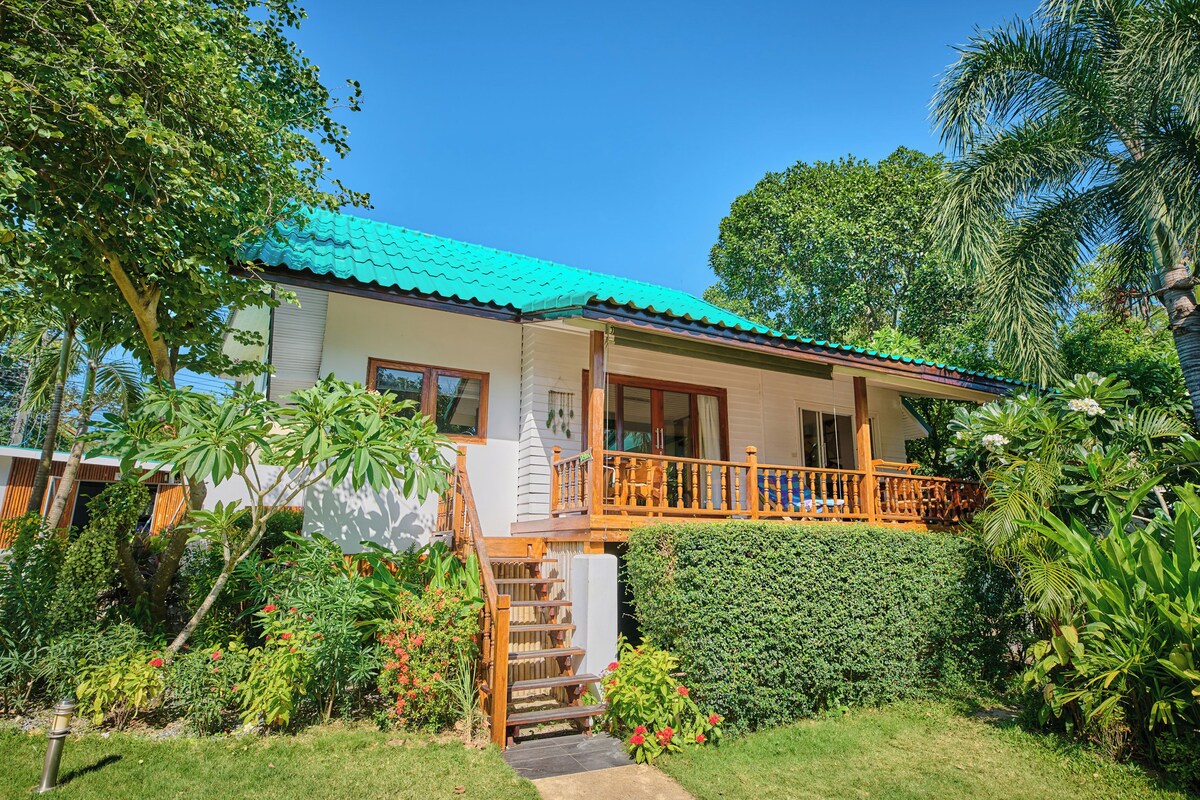 A two-story house with a green roof, a wooden balcony, and a well-maintained garden.