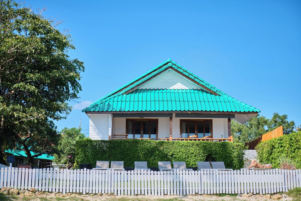 A two-story house with a green roof, white exterior walls, and a white picket fence.