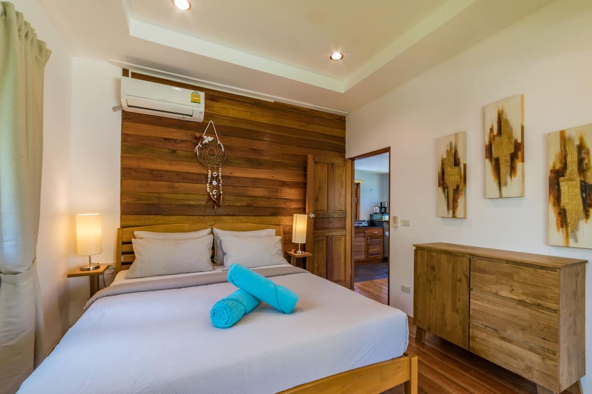 A hotel room with a wooden headboard, a bed with white bedding, a blue towel, a wooden dresser, and abstract paintings on the wall.