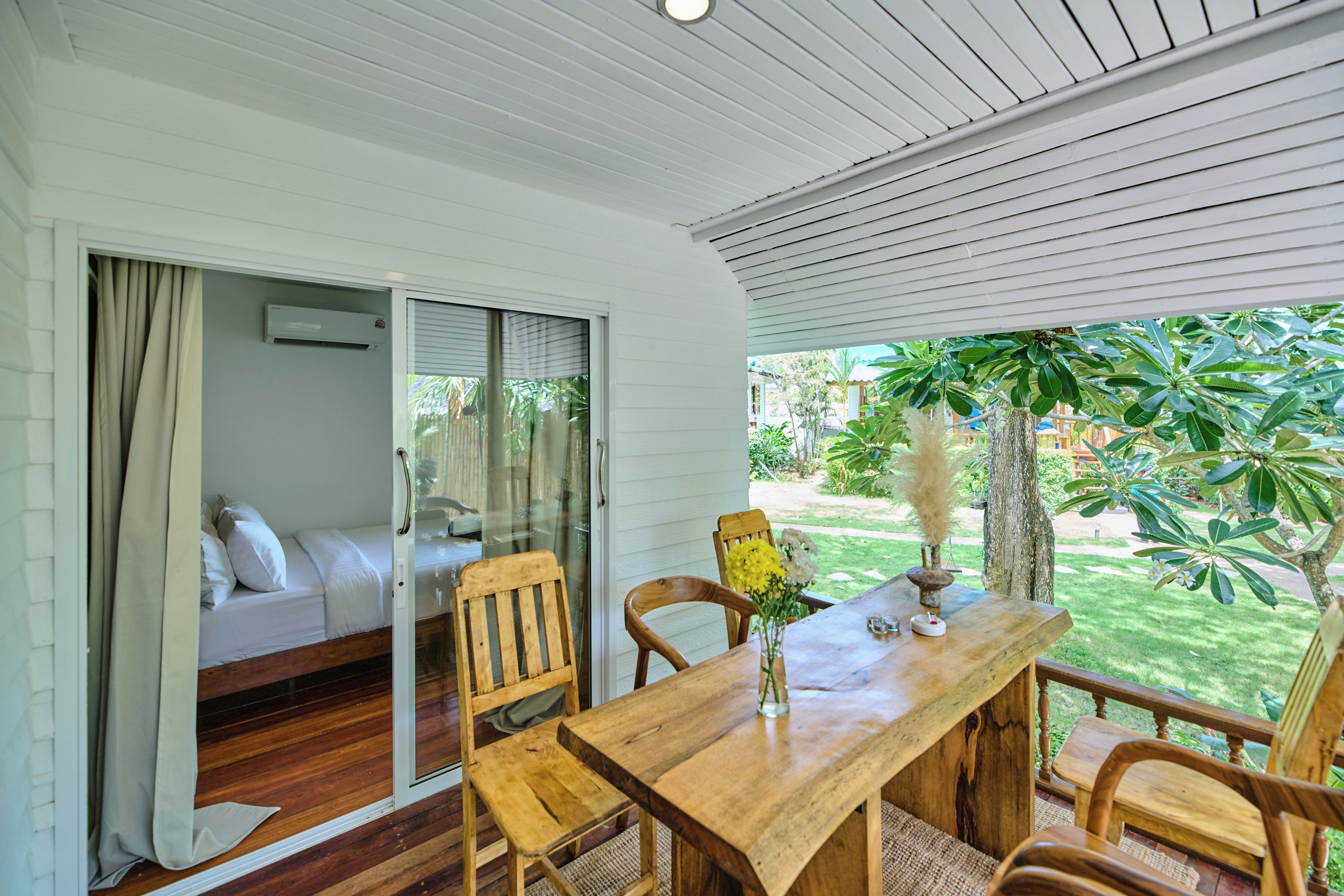A room with a wooden table, chairs, a sofa, and a sliding glass door leading to a garden.