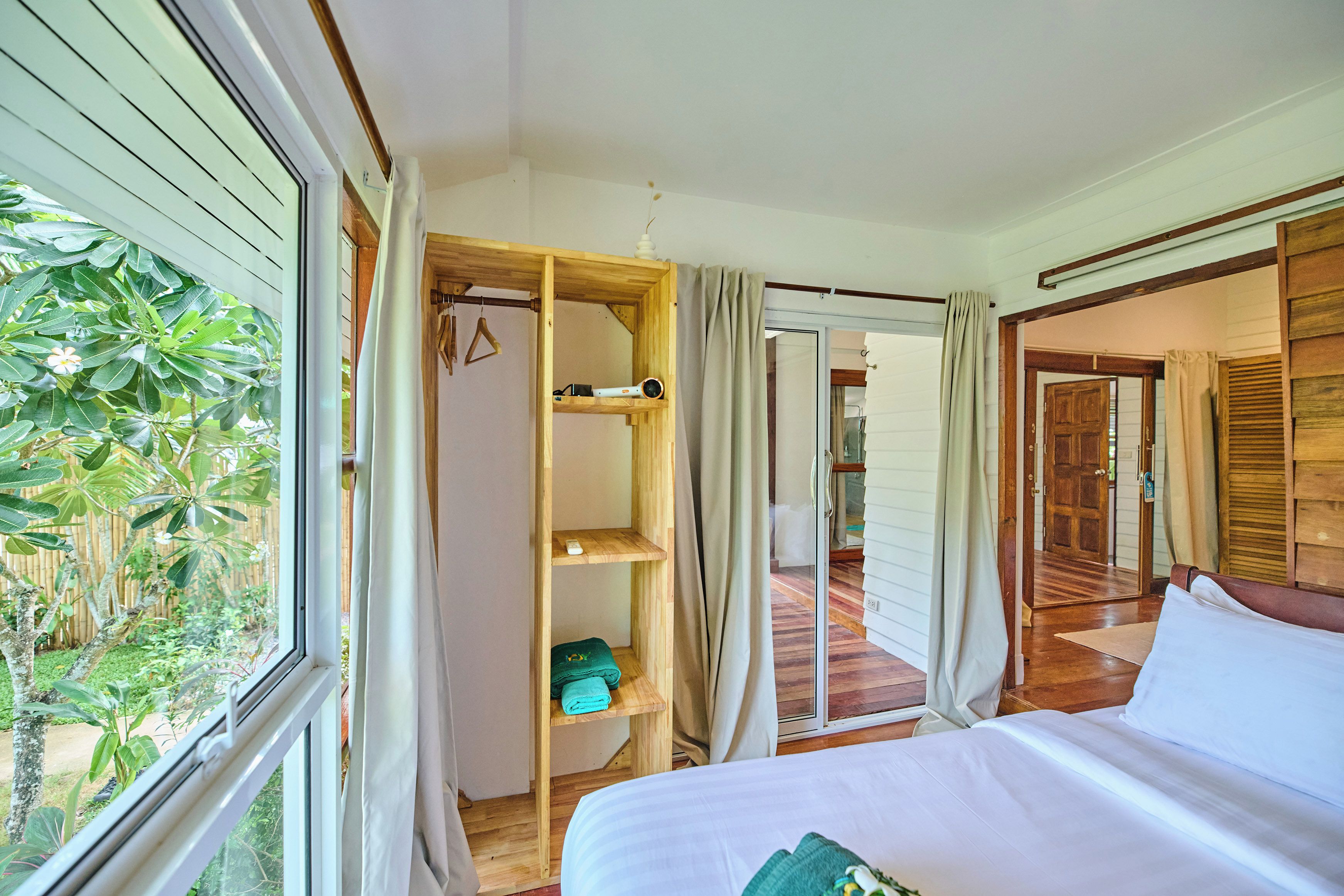 A bedroom with a bed, a wooden wardrobe, and a view of the outdoors.