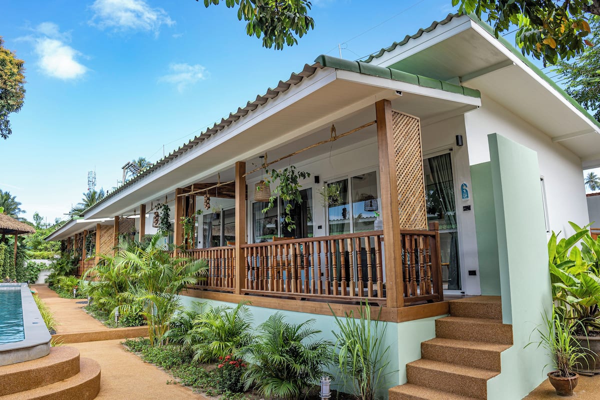 A two-story house with a covered porch, a swimming pool, and lush greenery.