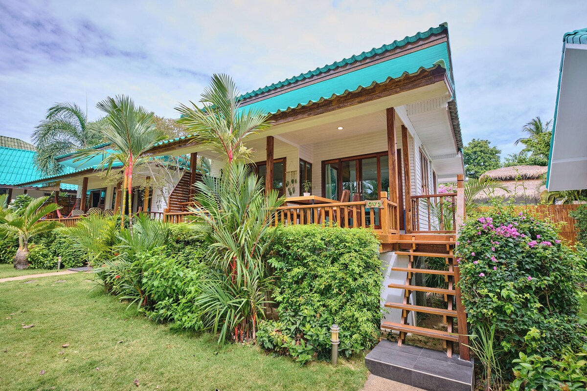 A two-story building with a covered porch, a staircase, and a well-maintained garden with various plants and a pathway.