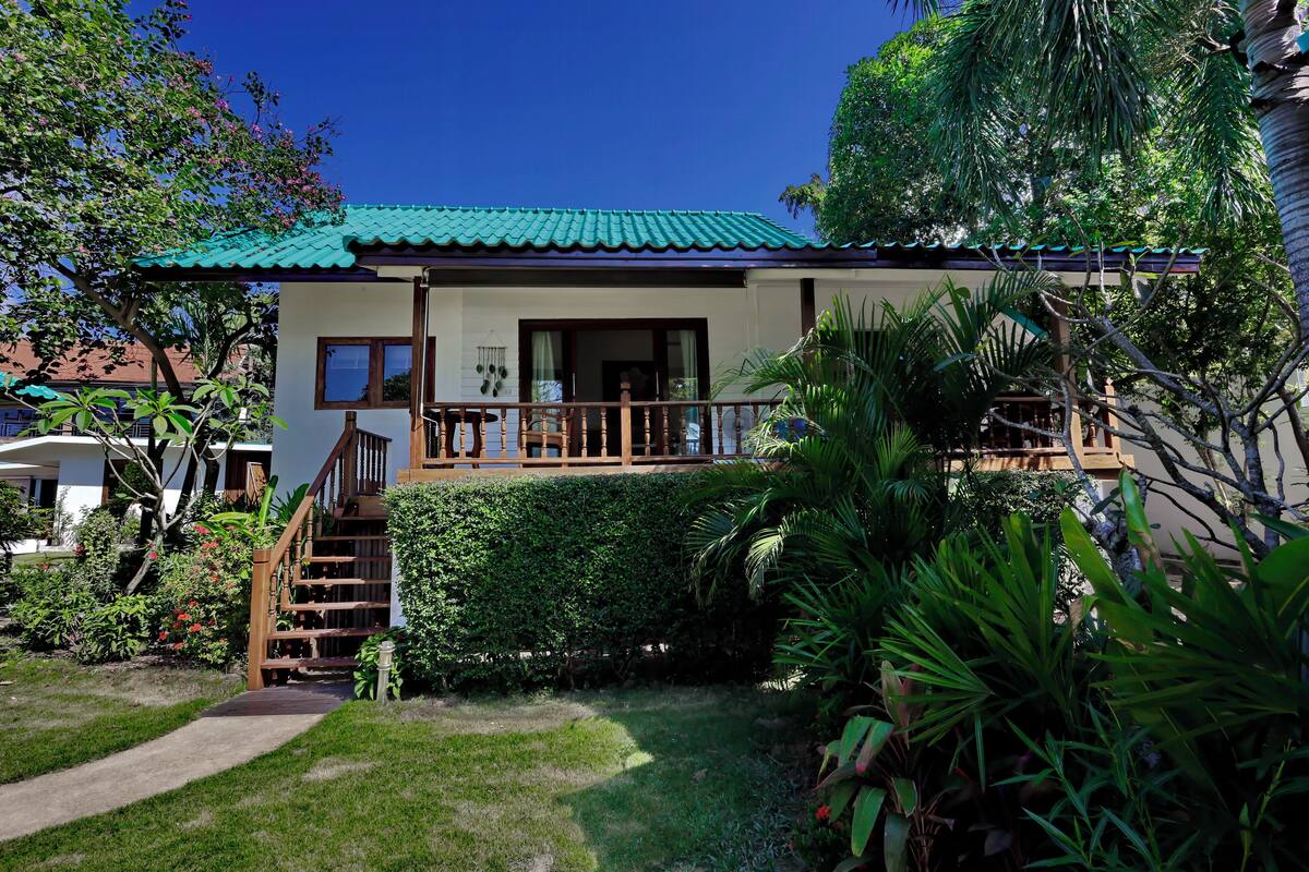 A two-story house with a green roof, a wooden staircase, and a balcony.