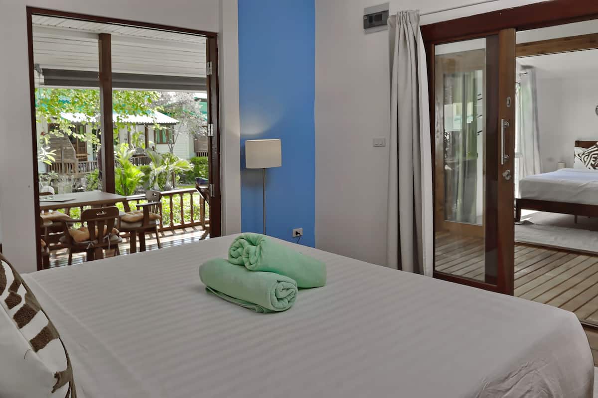 A hotel room with a bed, a balcony with a table and chairs, and a view of greenery outside.