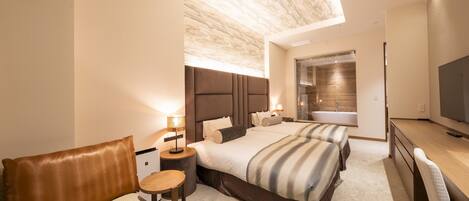 A modern hotel room with a large bed, a desk, and a bathroom with a glass shower.