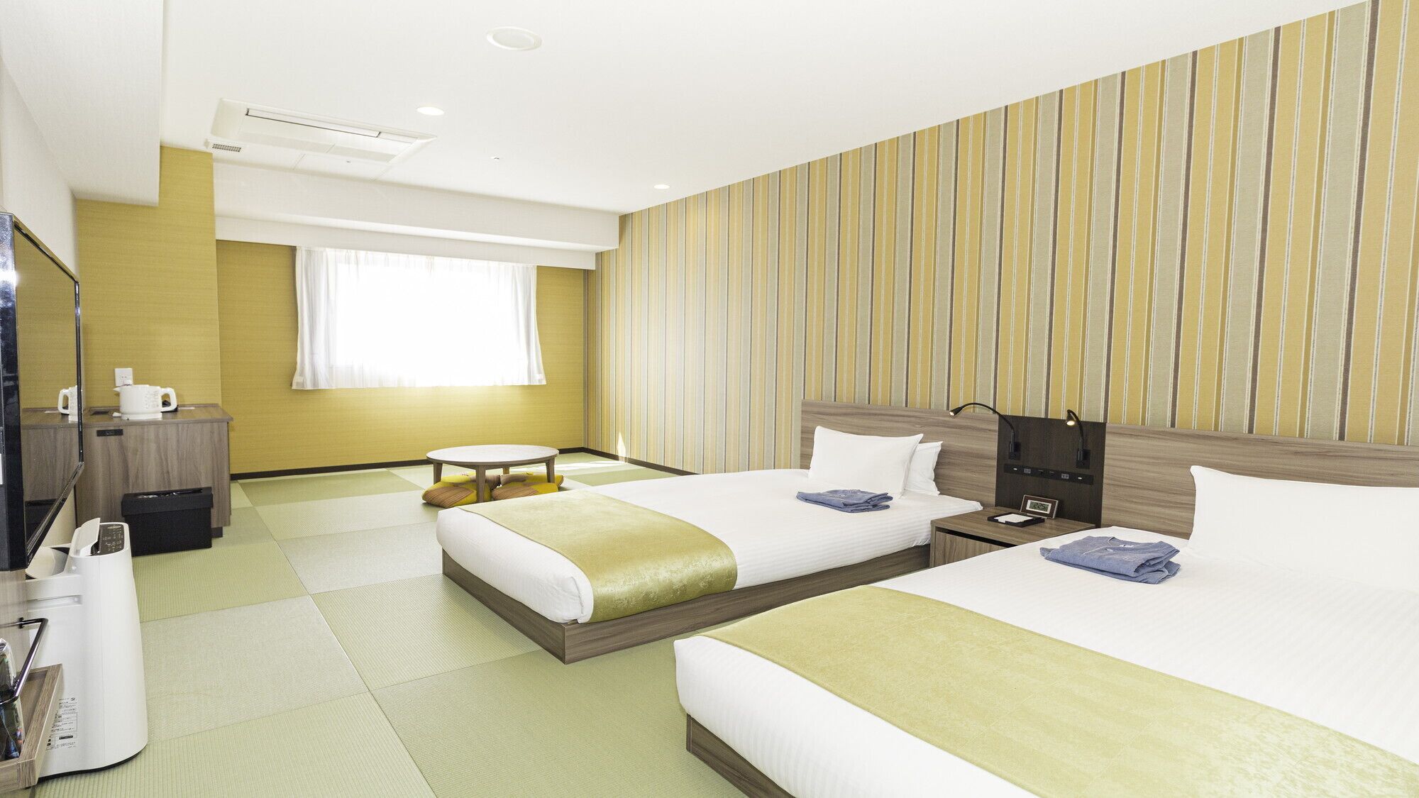 A hotel room with two beds, a small table, a desk with a telephone, and a window with curtains.