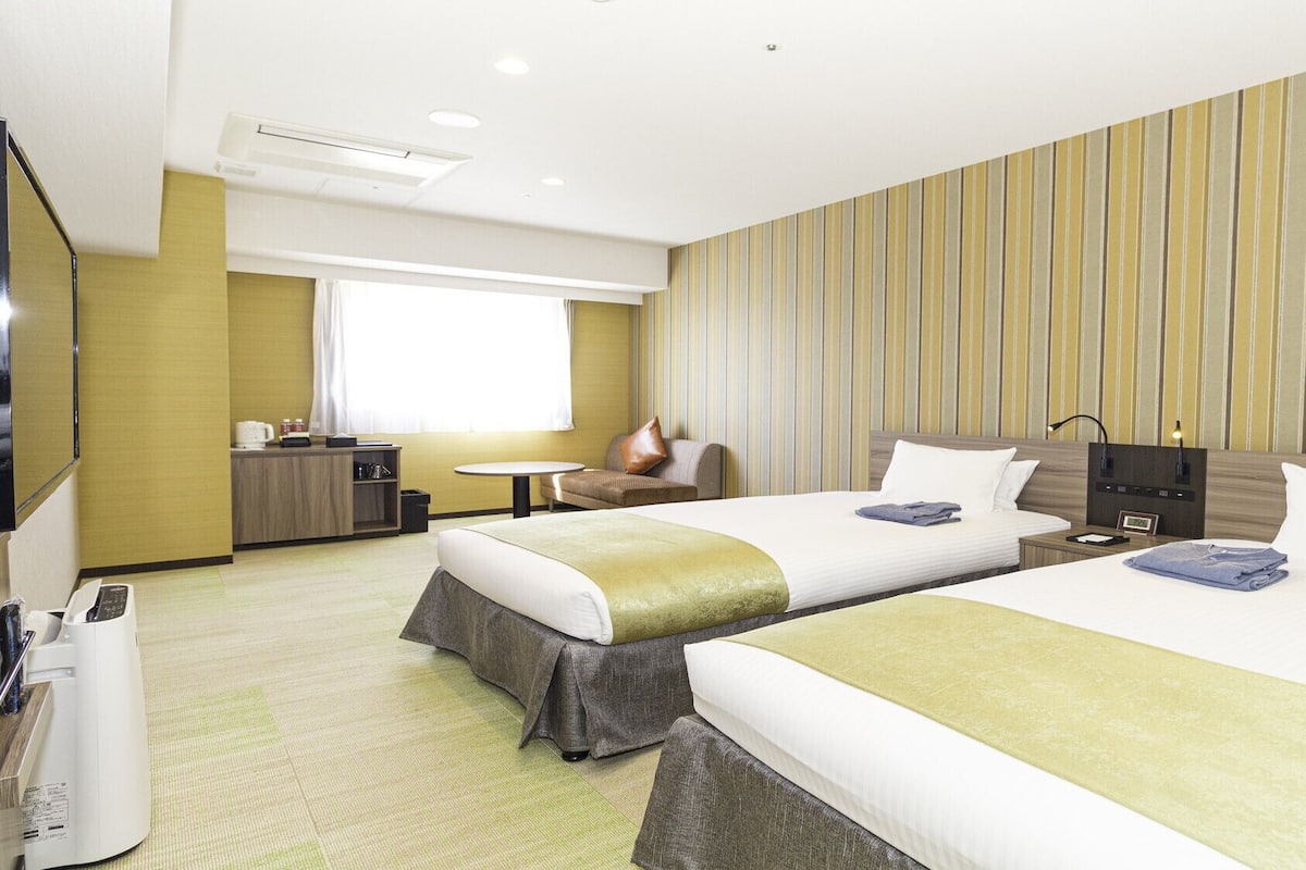 Habitación de hotel con dos camas, una mesita, un sofá, un televisor y un minibar.