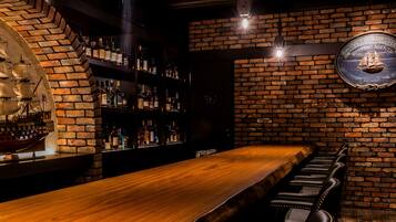 A bar area with a long wooden counter, leather barstools, and a brick wall with a shipping agents sign.