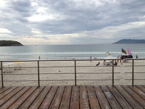 A beach with a wooden deck in the foreground, a sandy beach, and a calm sea.