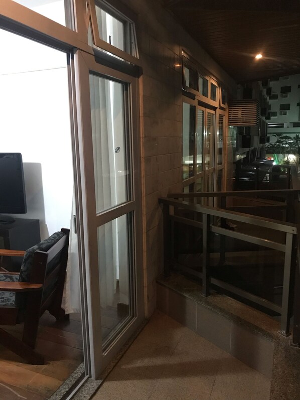 A modern interior with a glass door leading to a balcony, a seating area with a sofa and a table, and a staircase with a railing.