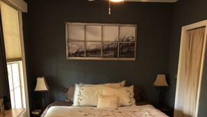 Un dormitorio con una cama grande, dos lámparas de noche, un ventilador de techo y una ventana con persianas.