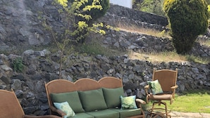 Un patio de piedra con un sofá de mimbre, dos sillones y una mesita.