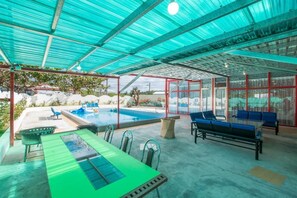 Ein überdachter Außenbereich mit Pool, Sitzgelegenheiten und einem Tisch.