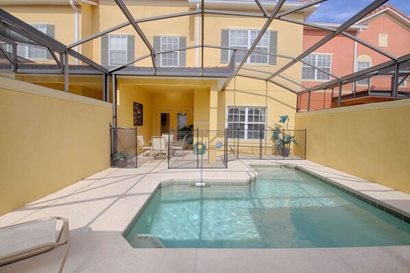 Relax by the pool surrounded by a glass-enclosed area with lounge chairs and a small table.