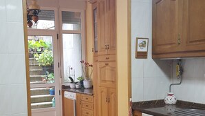 A kitchen with wooden cabinets, a tiled floor, and a window with plants. - Holiday apartment, downtown, seasons (Monforte de Lemos)