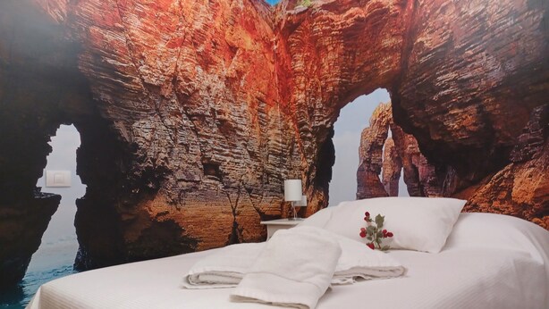 A bedroom with a large bed, white linens, a nightstand with a lamp, and a wall mural of a red rock formation. - Holiday apartment, downtown, seasons (Monforte de Lemos)