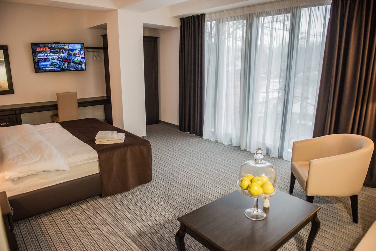 Hotelkamer met een bed, een tv waarop een menukaart staat, een tafel met een glazen stolp met citroenen, en een stoel.