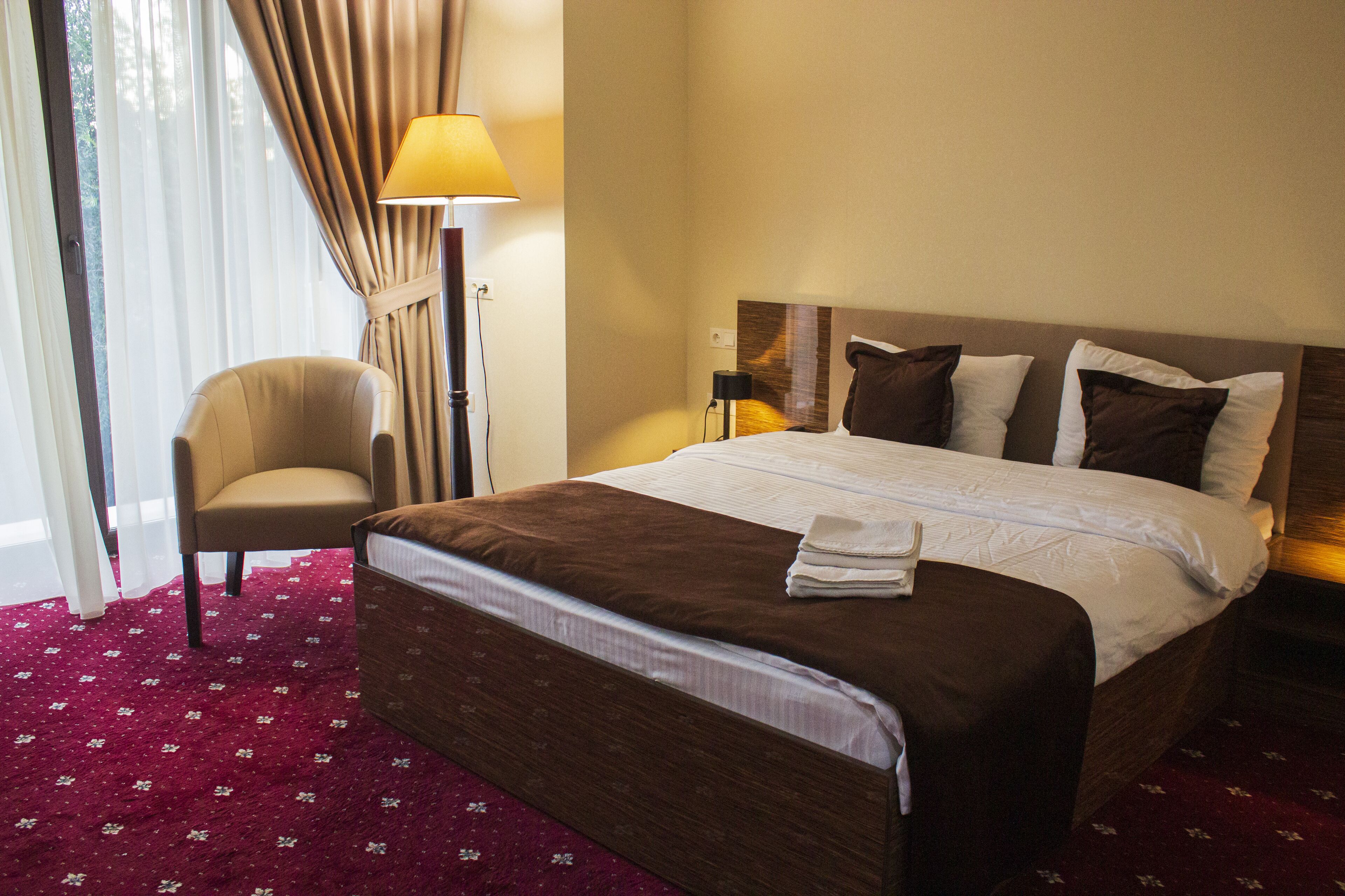 Une chambre d’hôtel avec un lit, une chaise, une lampe et une fenêtre avec des rideaux.