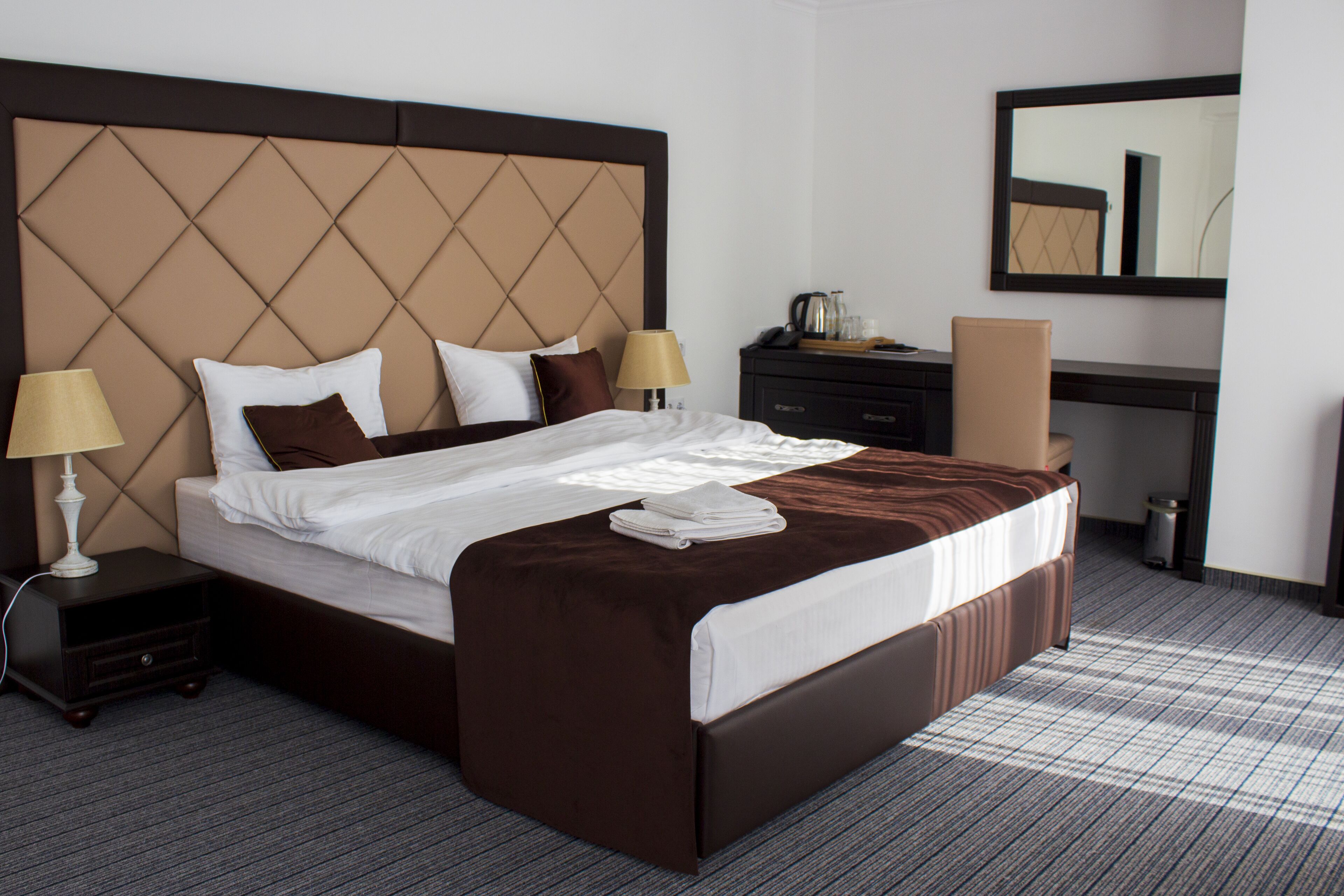 Habitación de hotel con una cama grande, dos mesitas de noche, un escritorio y un espejo.