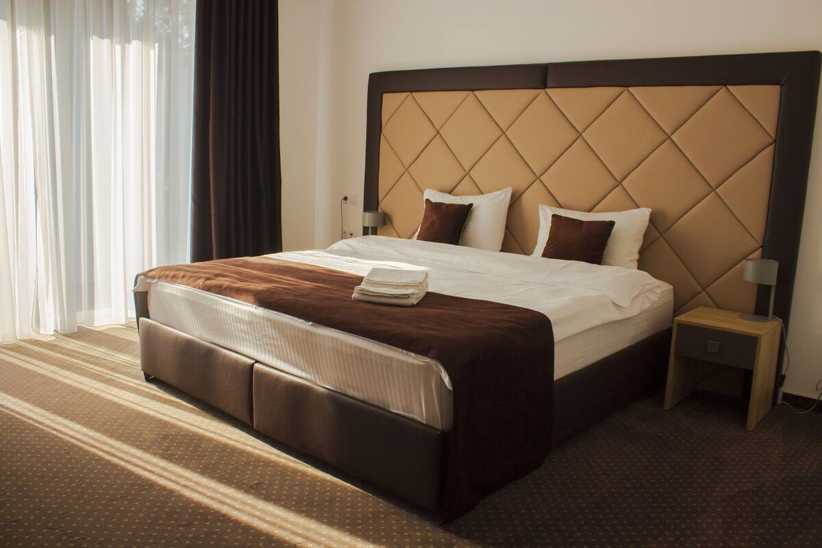 Een hotelkamer met een groot bed, nachtkastje en een raam met gordijnen.