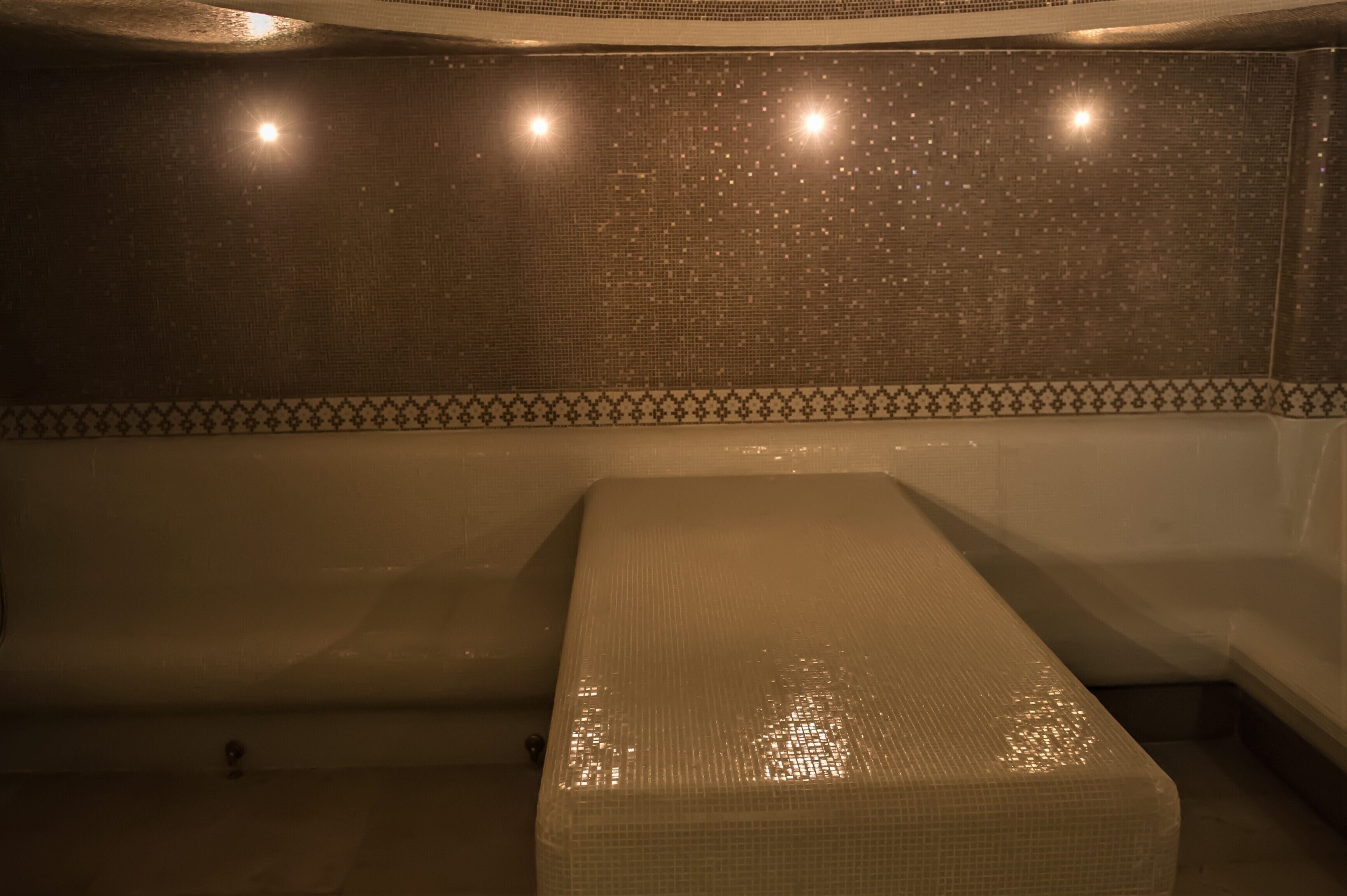 A room with a bathtub, a small bed, and a tiled wall with a decorative border.