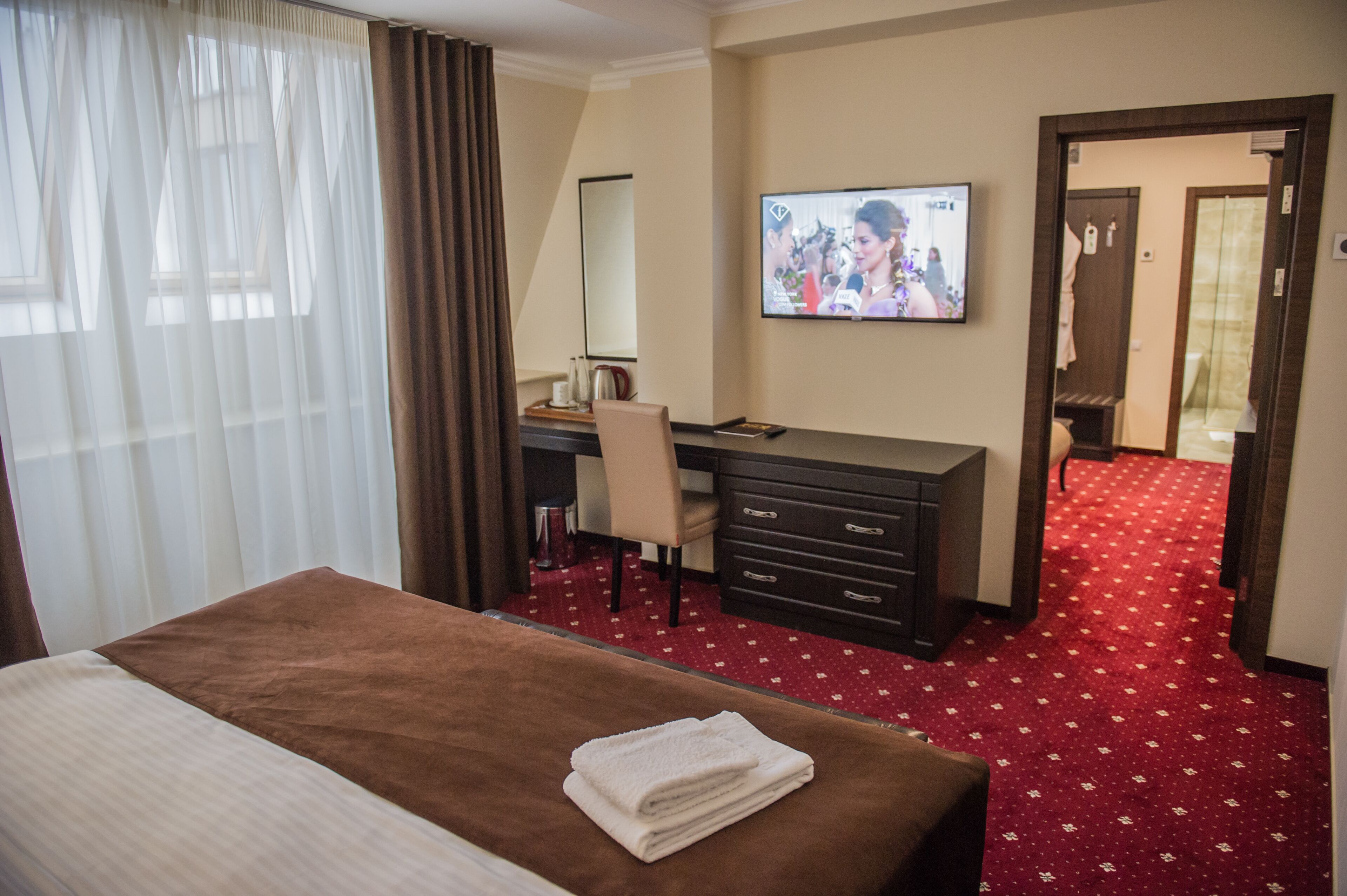 A hotel room with a bed, a desk, a television, and a red carpeted floor.