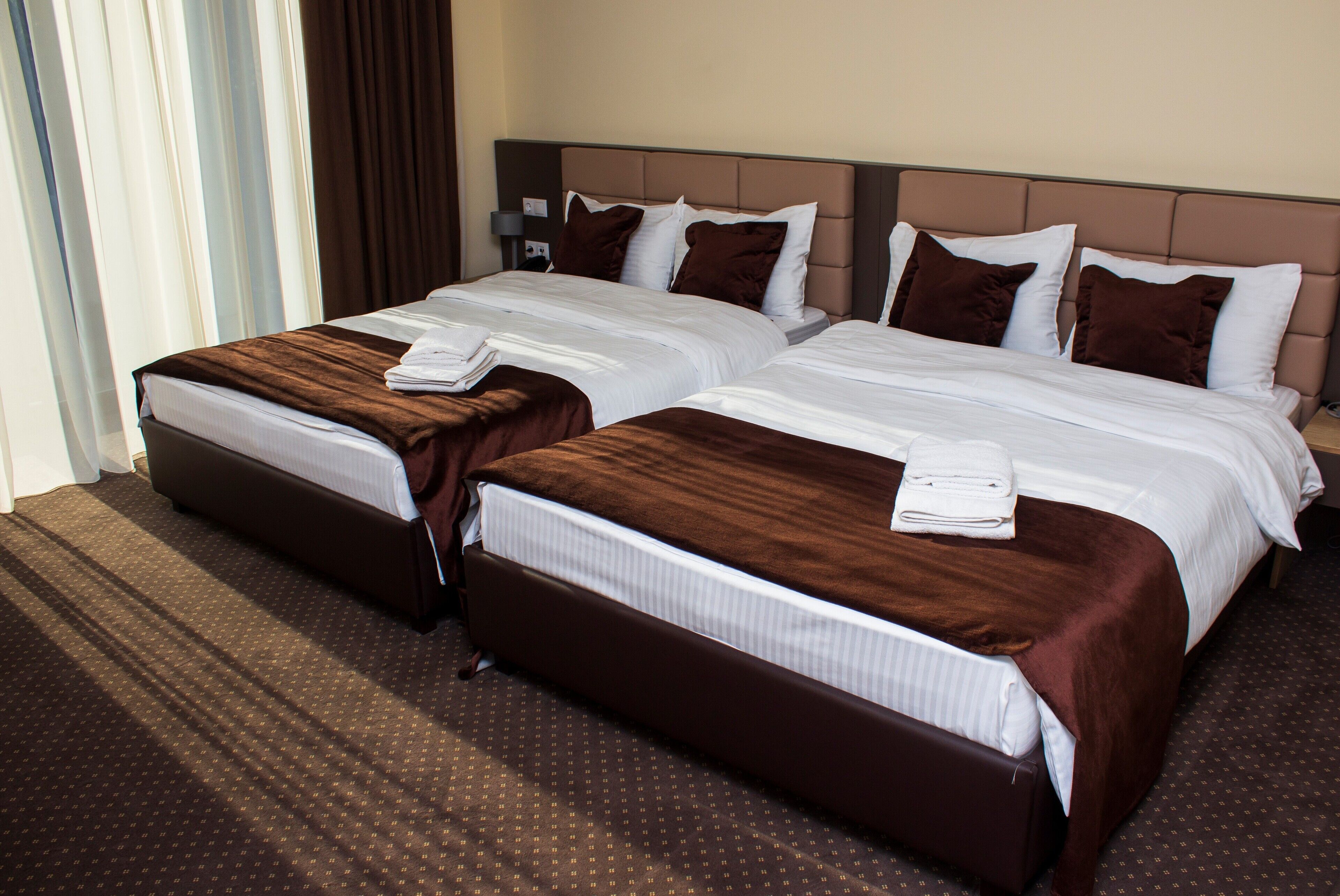 Habitación de hotel con dos camas, cada una con cabecero marrón, ropa de cama blanca y una manta marrón.