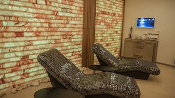 A spa area with two reclining chairs, a massage table, and a television on the wall.