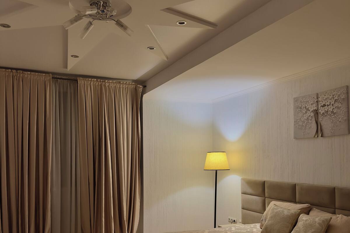 Een slaapkamer met een bed, een plafondventilator, een lamp en een schilderij aan de muur.