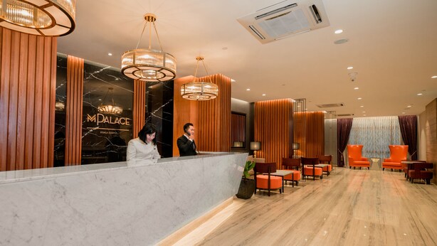A hotel reception area with marble counters, modern chandeliers, and a seating area with orange chairs. - M Palace Hotel (Kuala Lumpur)