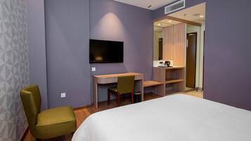 A hotel room with a bed, a desk, a chair, a television, and a bathroom visible through an open door.