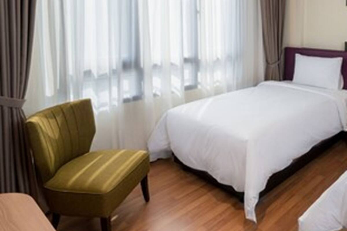 A hotel room with a bed, a chair, and a window with curtains.
