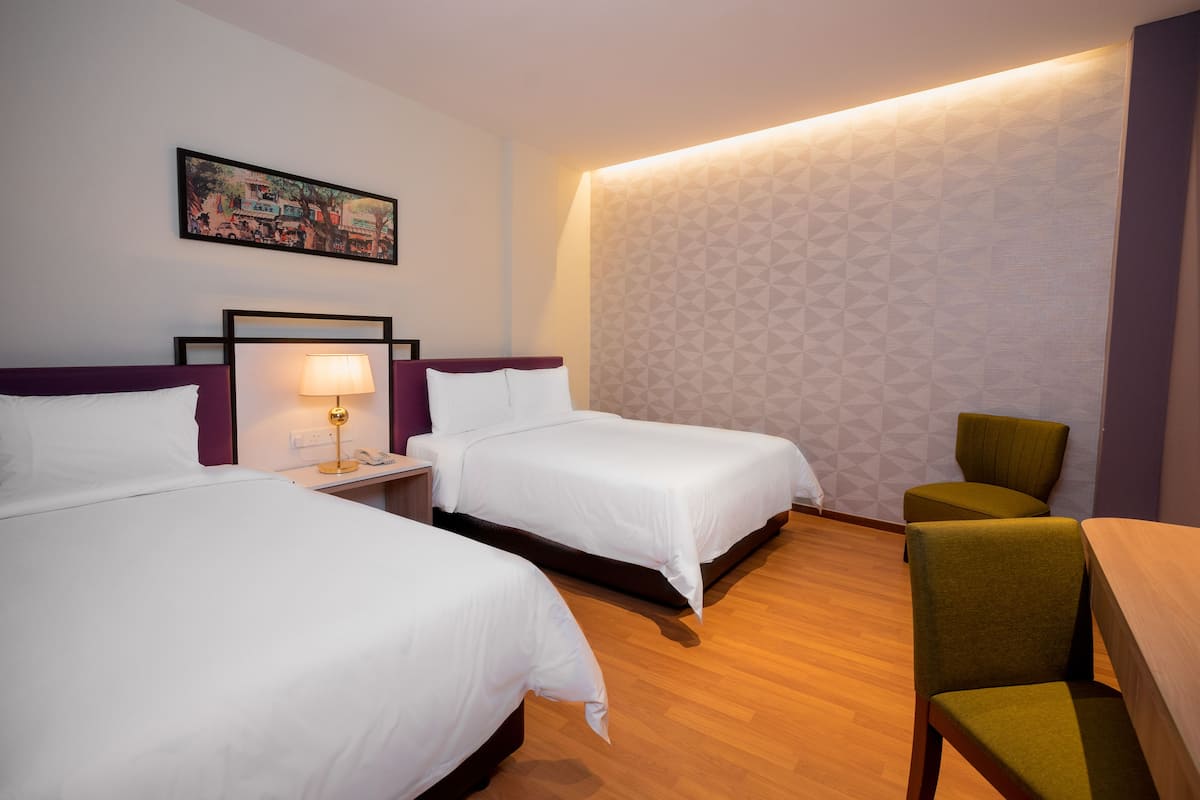 A hotel room with two beds, a nightstand with a lamp, a chair, and a wall-mounted picture.