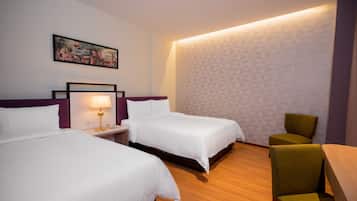 A hotel room with two beds, a nightstand with a lamp, a chair, and a wall-mounted picture.