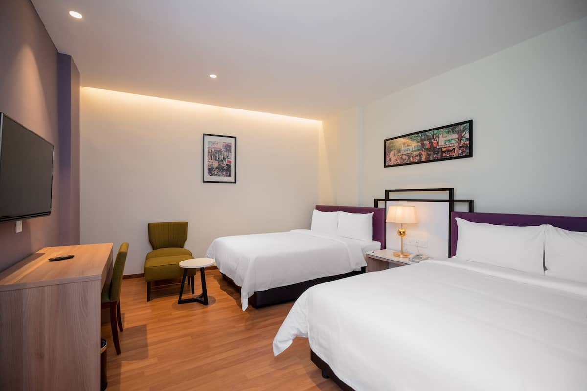 A hotel room with two beds, a desk, a chair, and a TV.